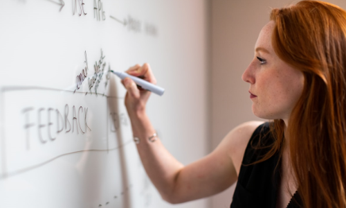 a woman writing on a whiteboard, possibly engaging in brainstorming, planning, or teaching
